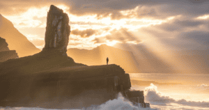 Psalm 61:2 meaning — silhouette on a high rock in morning light above misty waves